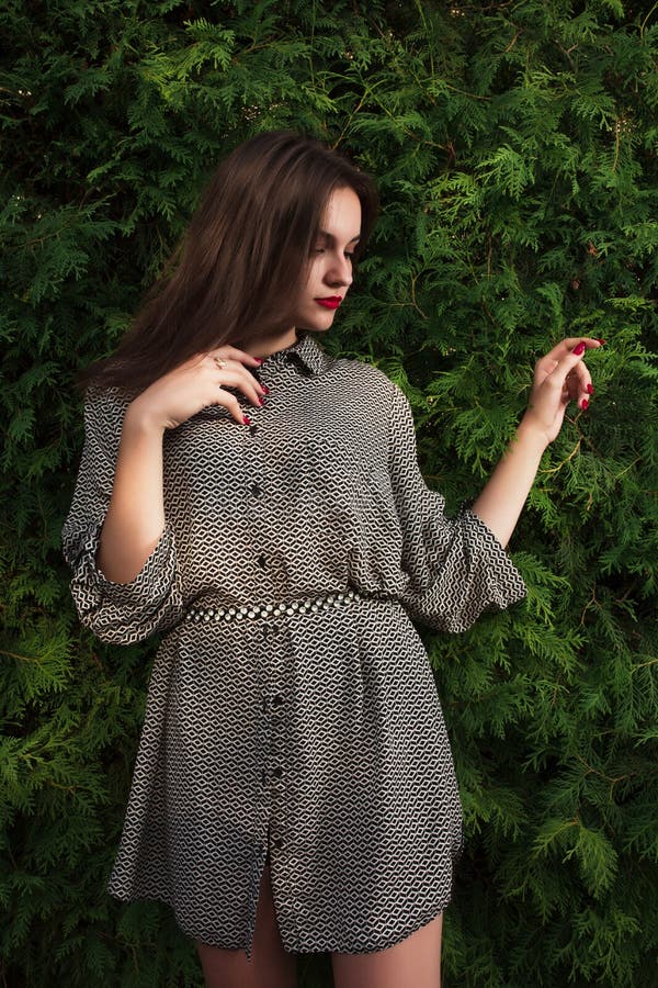 Fashionable brunette woman in casual shirt posing on a green thu