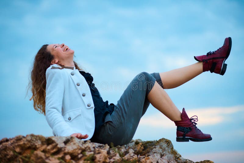 Fashionable girl dressed in white jacket and wide trousers posing at sunset sky background, sits on the stone royalty free stock photos Fashionable girl dressed in white jacket and wide trousers posing at sunset sky background, sits on the stone royalty free stock photos