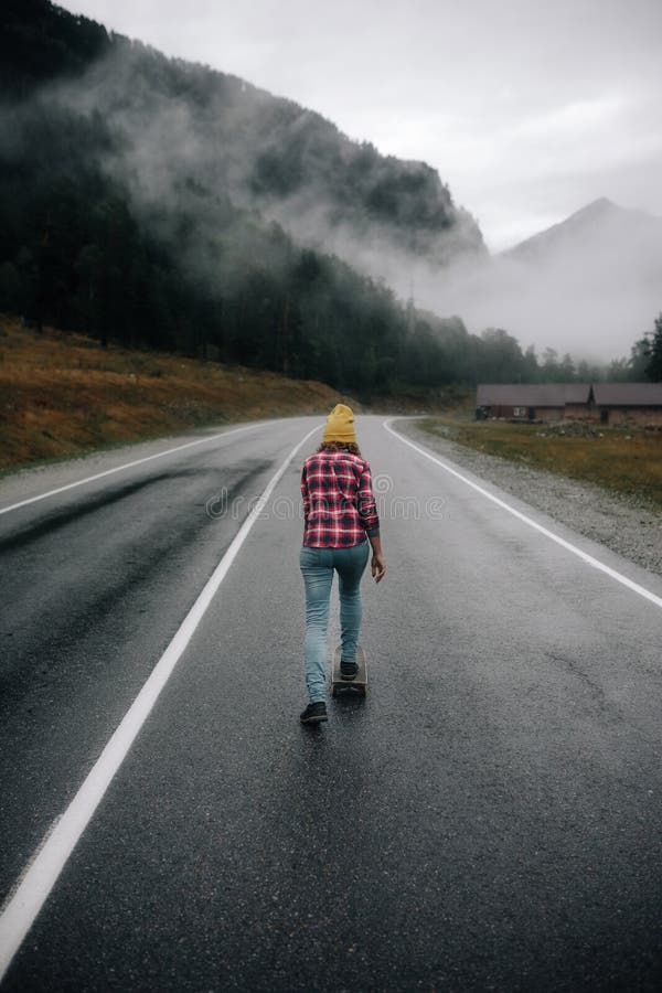 Fashionable hipster girl rides a skateboard on the road in the mountains around the mountain and beautiful view stock photography Fashionable hipster girl rides a skateboard on the road in the mountains around the mountain and beautiful view stock photography