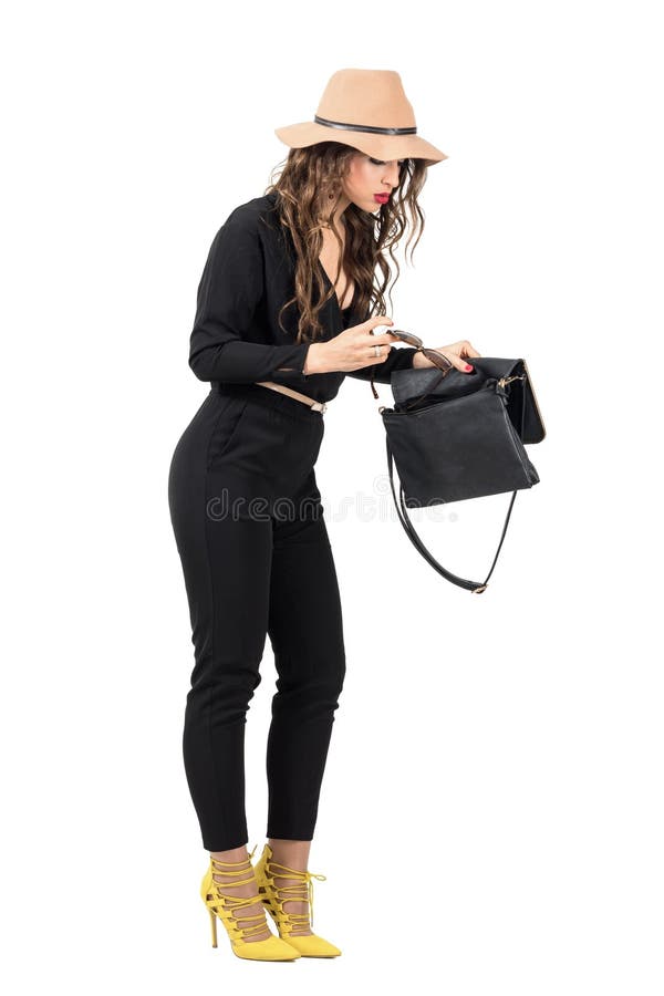 Fashionable woman in black overalls searching for something lost in her handbag