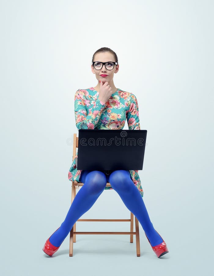 Fashionable young woman in dress and glasses sitting on chair with a laptop stock photography Fashionable young woman in dress and glasses sitting on chair with a laptop stock photography