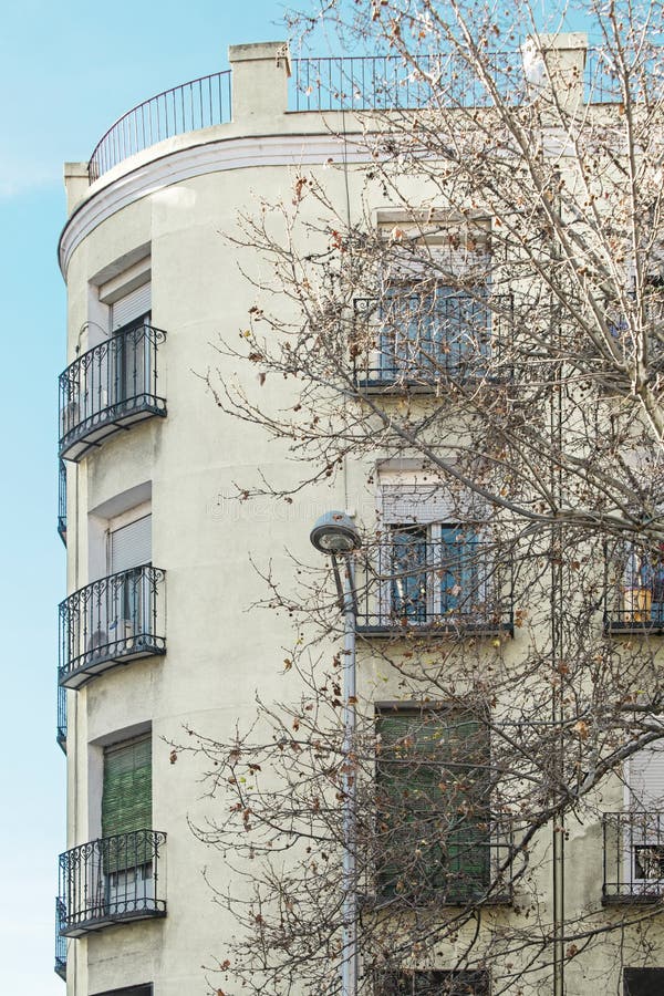 Fassade eines Gebäudes mit einer abgerundeten Ecke mit vielen Balkonen und Laubbäumen ohne Blätter lizenzfreie stockbilder