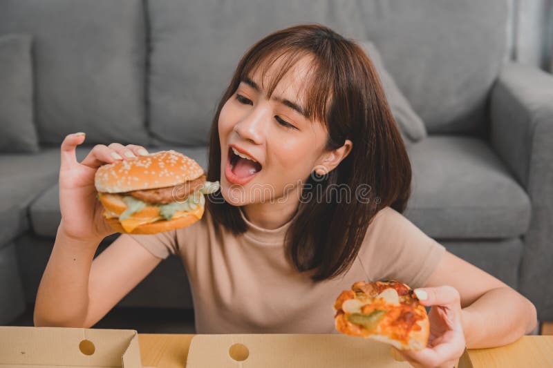 Fast food takeaway back home. Eating burger when takeout and delivery. Asian woman lifestyle in living room. Social distancing