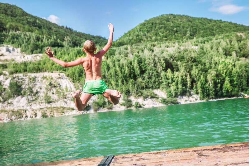 Fast running Boy jumping into  mountain lake from the dock. Careless childhood concept image