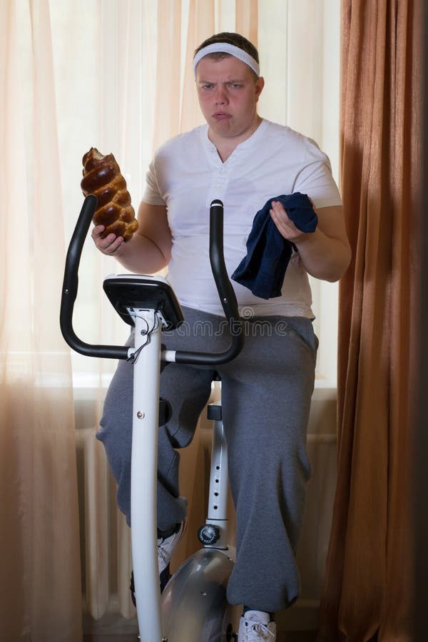 Fat Guy Exercising on Stationary Training Bicycle and Eating a Bun Stock Image Image of active