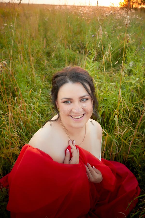 Fat Plump Chubby Pleasant Woman Or Girl In Elegant Red Dres In Green Grass Field Model Posing
