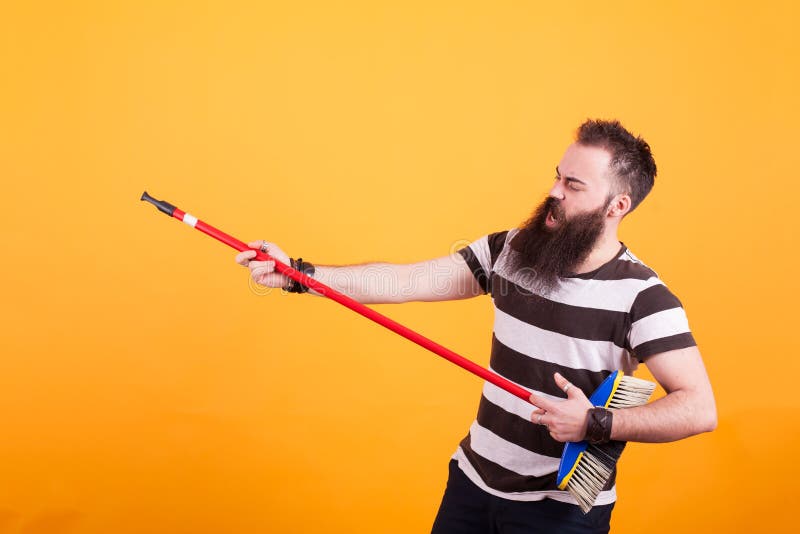 Fat young man picking up a broom as if it were a guitar