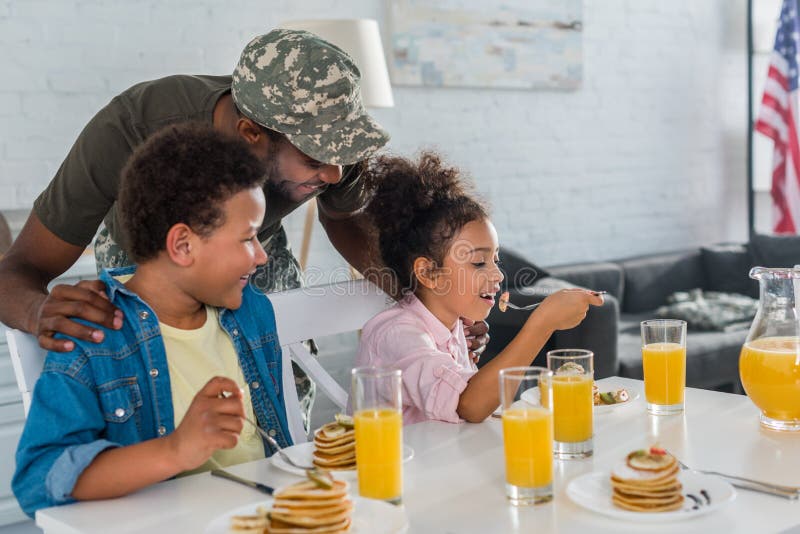 Father in army uniform and african american kids eating breakfast with pancakes