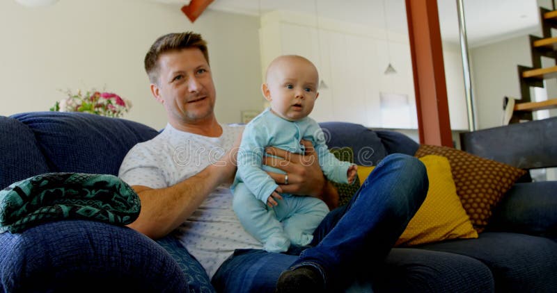 Father and baby boy watching television in living room 4k