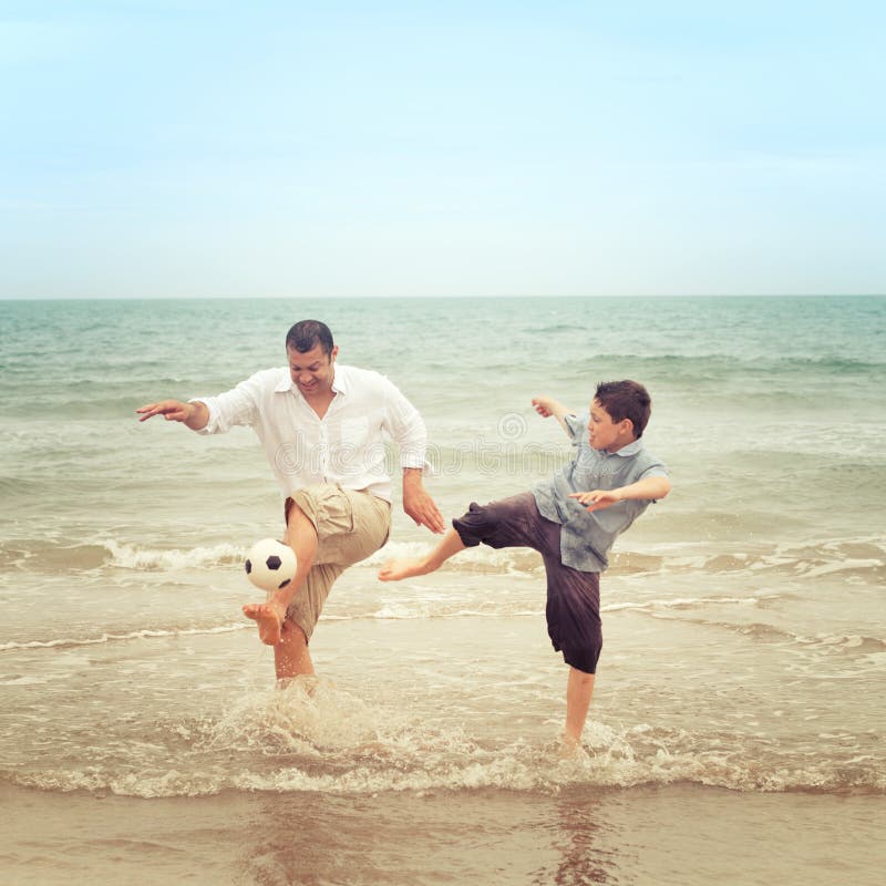 Father on beach kicking the ball while his son tries to get it