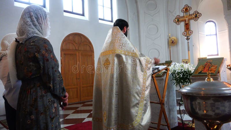 Father in a cassock recites a prayer at the baptism of a baby