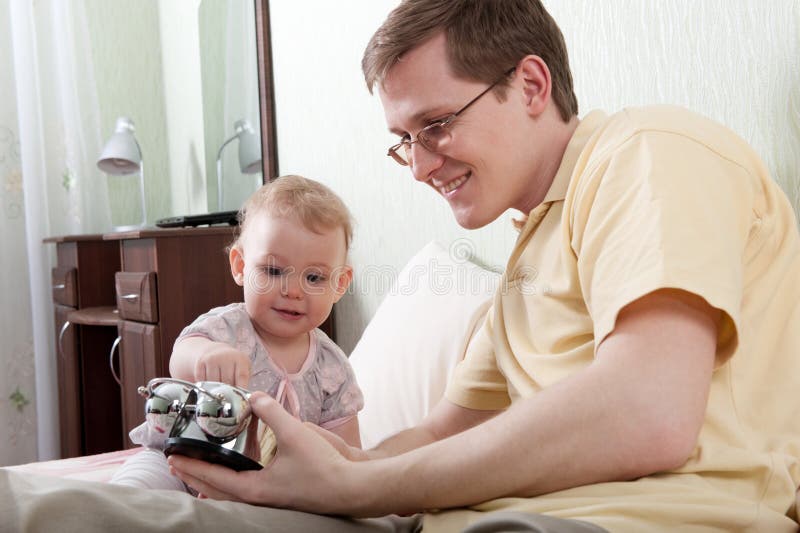 Father and daughter. Young father showing alarm clock to his little daughter Father and daughter. Young father showing alarm clock to his little daughter