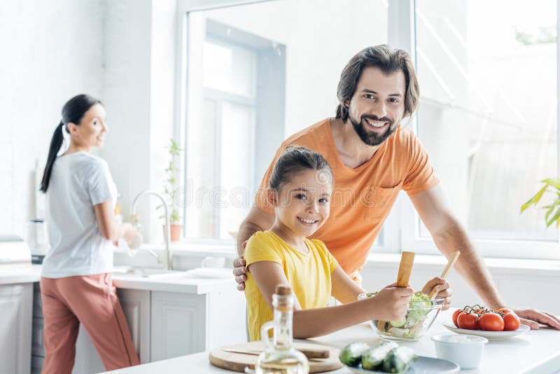 Father And Daughter Cooking Together While Mother Washing Dishes ...