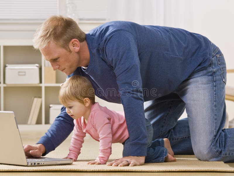 Father and Daughter with Laptop. A father uses a laptop while his baby daughter watches. Both are on all fours in their living room. Horizontally framed shot Father and Daughter with Laptop. A father uses a laptop while his baby daughter watches. Both are on all fours in their living room. Horizontally framed shot