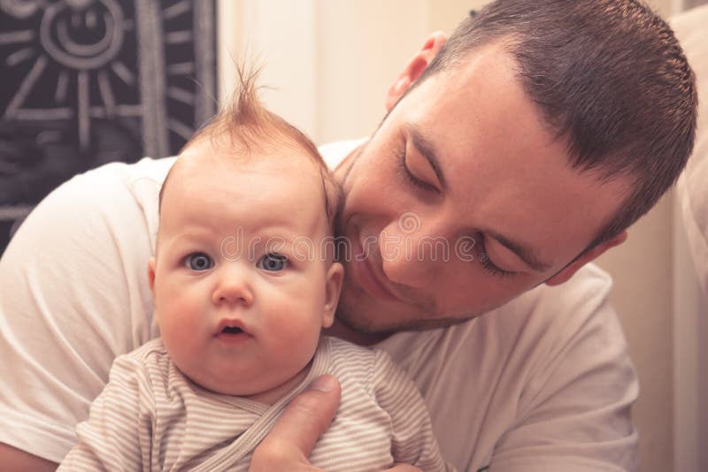 Father embracing his little baby. Father is looking on baby, baby is looking on camera. Baby with funny haircut