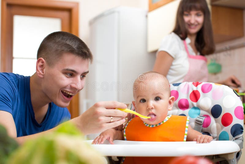 Father feeding his kid and mother cooking at kitchen stock photography Father feeding his kid and mother cooking at kitchen stock photography