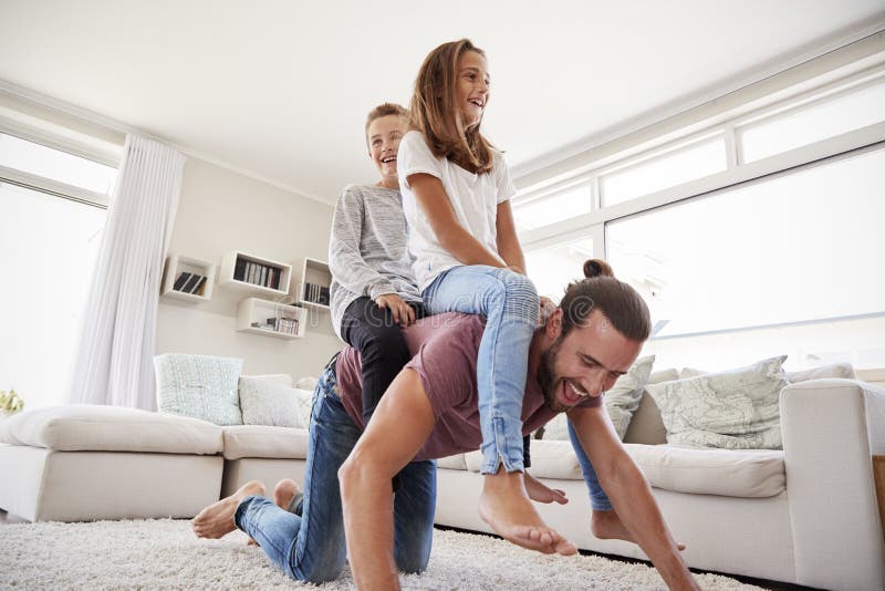 Father Giving Children Ride On Back In Lounge At Home. 