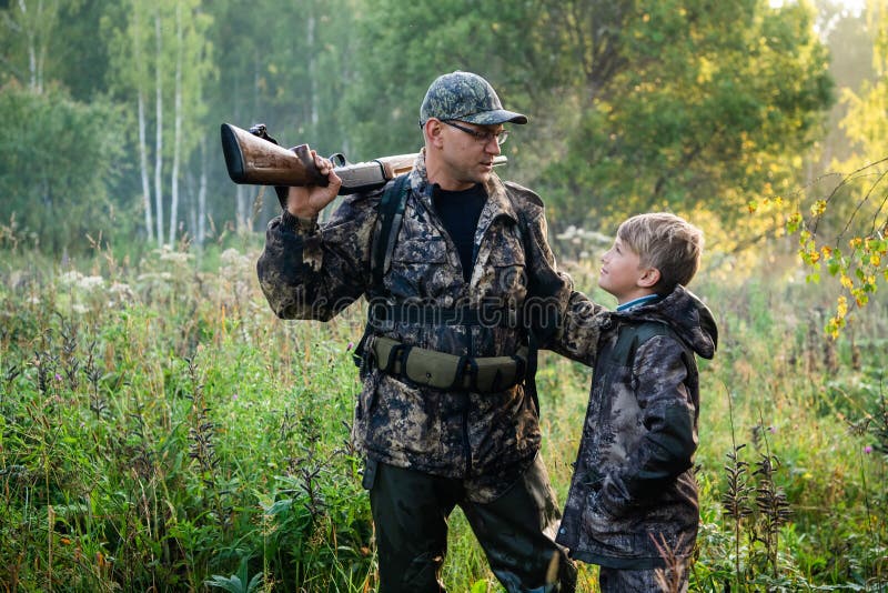 Father with gun showing something to son while hunting on a nature.