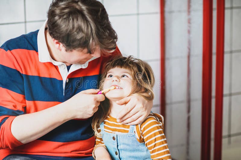 Father helping his little daughter with brushing teeth. Little toddler girl and dad in bathroom, making hygiene actions