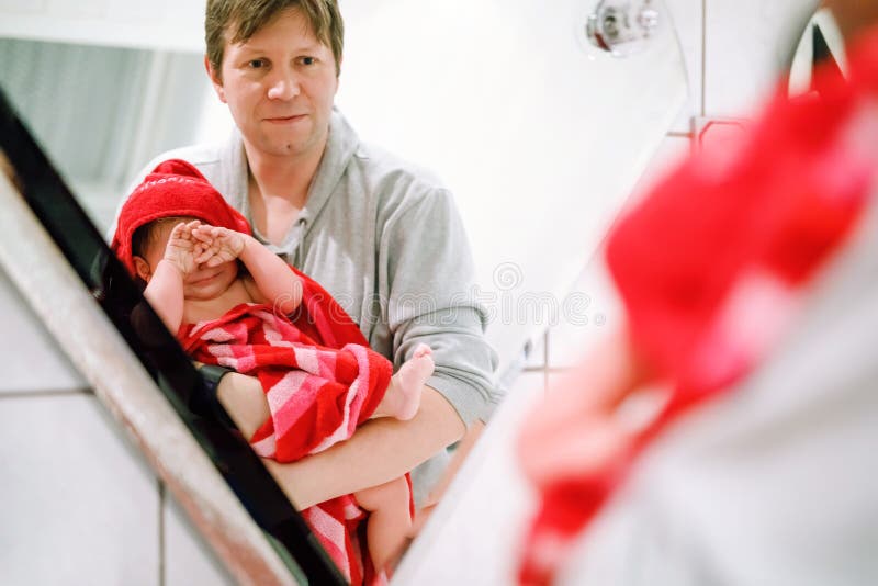 Father holding cute little toddler girl wrapped in towel after taking bath. Happy healthy baby child with wet hairs