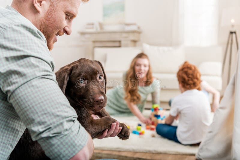 Father holding labrador retriever puppy, happy family behind at home
