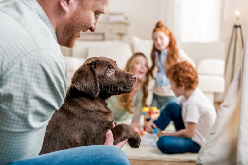 Father holding labrador retriever puppy, happy family behind at home