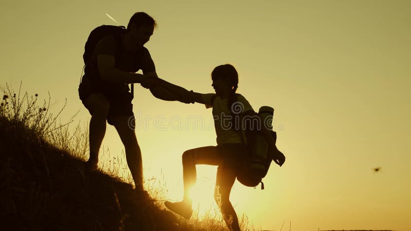 Father holds out his hand helping children climb mountain. Family of tourists with kids traveling at sunset. dad