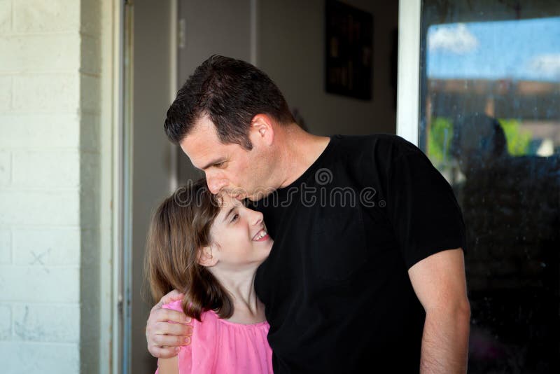 A father kisses his daughter on the forehead as he hugs her and pulls her c...