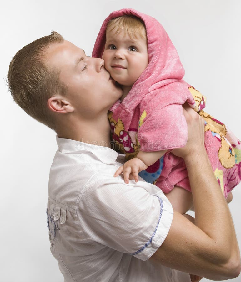 Sorridente, felice, giovane padre di baciare e abbracciare il suo bambino sveglio figlia che indossa una rosa bathcoat.