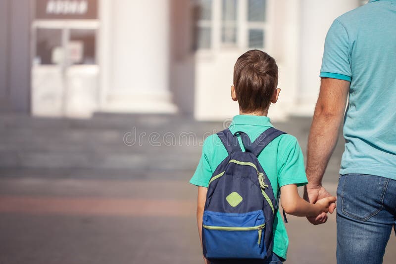 Father leads a little child school boy go hand in hand. Parent and son with backpack behind the back royalty free stock photography