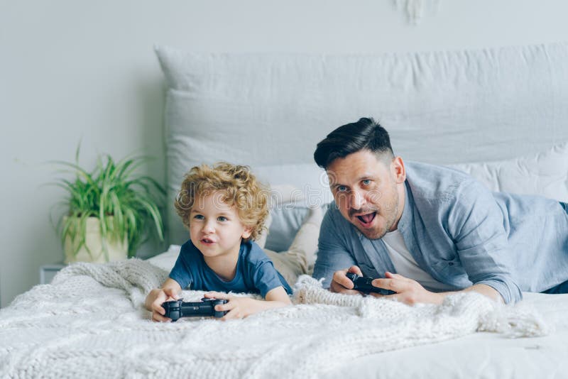 Father and child playing video game on bed at home pressing buttons on joystick royalty free stock photos Father and child playing video game on bed at home pressing buttons on joystick royalty free stock photos