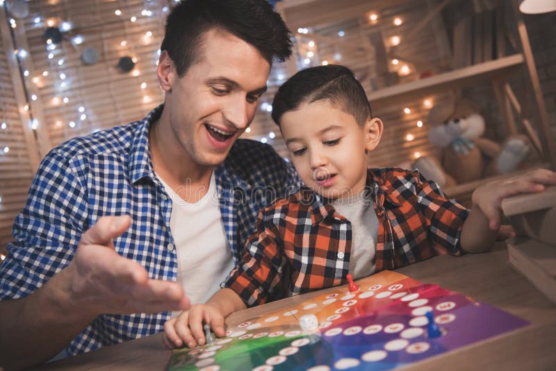 Father and little son are playing board game at night at home.