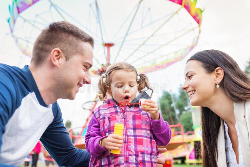 Father, mother, daughter blowing bubbles, amusement park, fun fa stock phot...