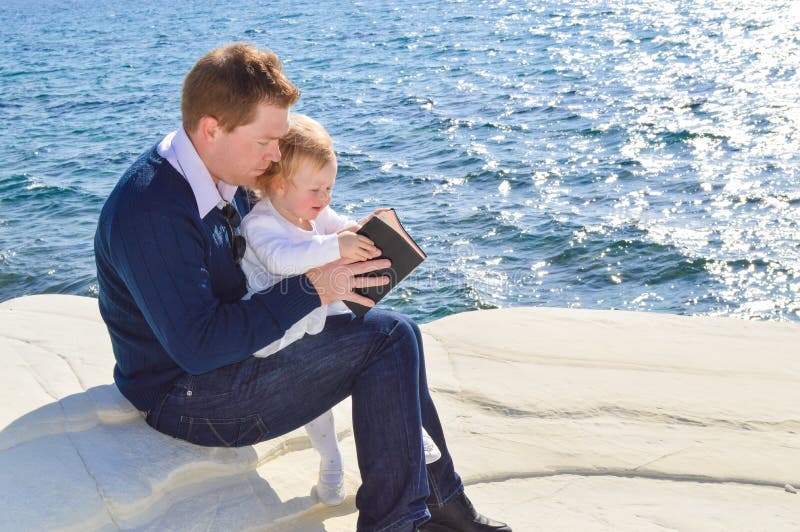 Father reading The Bible to his daughter by the sea