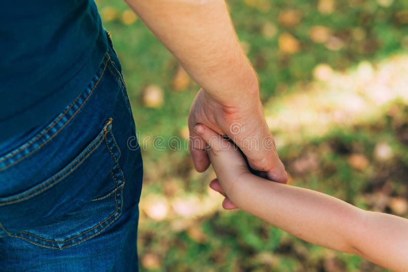 Father`s day. Dad and son. Dad holds the hand of a little son in the park. Little child holding hands with his father outdoors. stock photo Father`s day. Dad and son. Dad holds the hand of a little son in the park. Little child holding hands with his father outdoors. stock photo