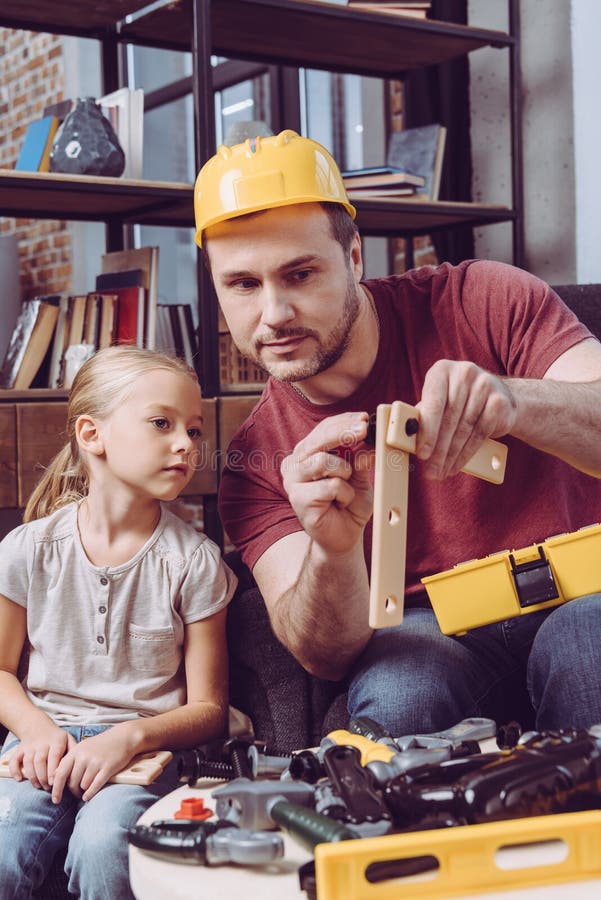 Father showing his daughter how to make a wooden frame with different toy tools at home stock photography Father showing his daughter how to make a wooden frame with different toy tools at home stock photography