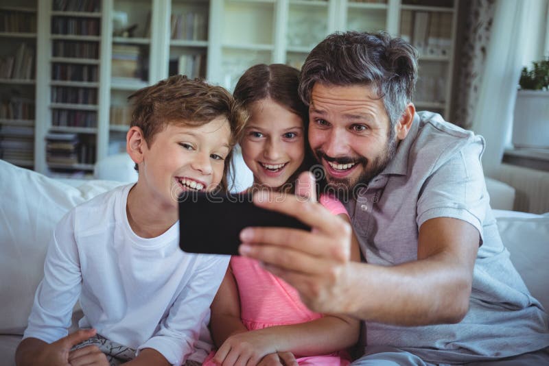 Father sitting on sofa with his children and clicking a selfie in living room