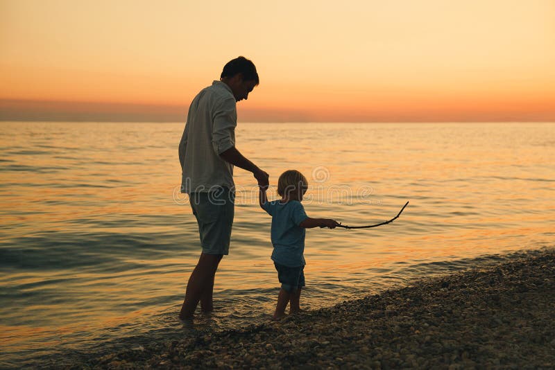 Father and son back silhouettes walking by the sea. stock photo Father and son back silhouettes walking by the sea. stock photo