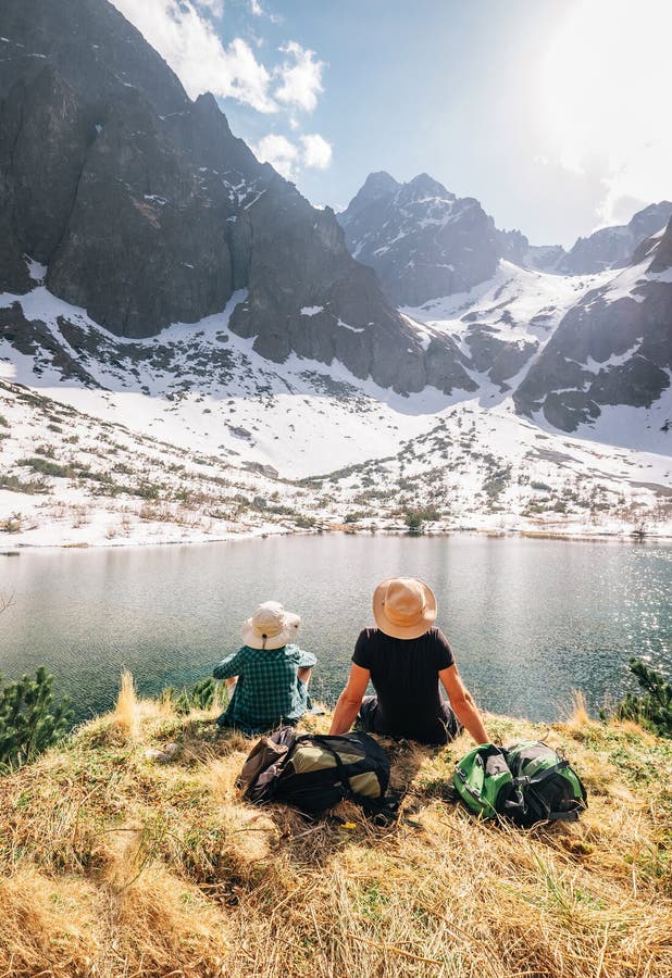 Father and son backpackers resting near the mountain lake Zelene Pleso in Slovakia and enjoying snowy peaks. Spring-summer hiking