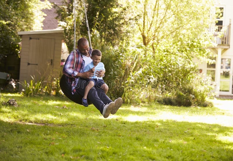 Father And Son Having Fun On Tire Swing In Garden