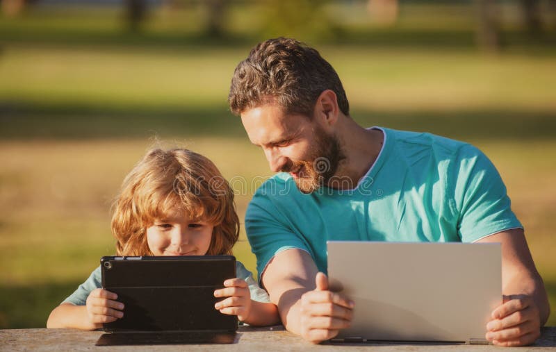 Father and son with laptop and tablet. Online learning. Kid with a laptop outdoors in the summer. Child in a park on