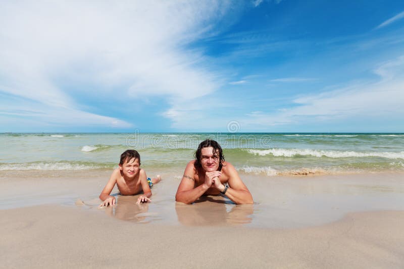 Father and son lying on the sandy beach.