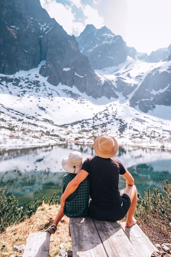 Father and son resting near the mountain lake and enjoying the snow mountains and water surface beauties. Active leisure, spring