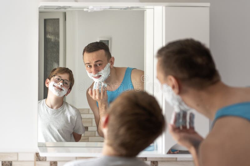 Father and son shaving in bathroom together and having fun. Dad and son in bathroom in front of mirror