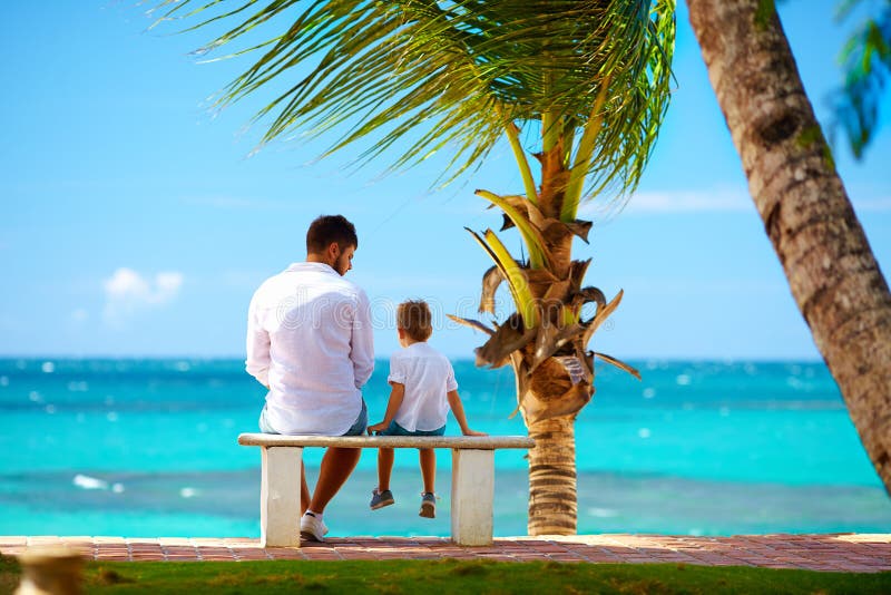 Father and son sitting on bench in front of the ocean