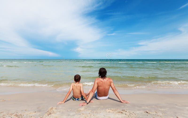 Father and son sitting on the sandy beach.