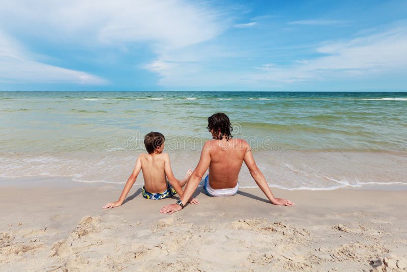 Father and son sitting on the sandy beach.