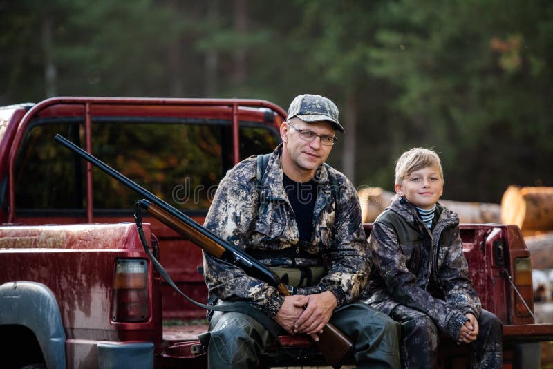 Father and son sitting together in truck outdoors with shotgun hunting gear.