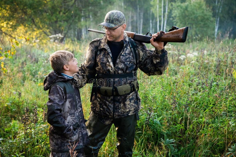 Father and son standing together outdoors with shotgun hunting gear.