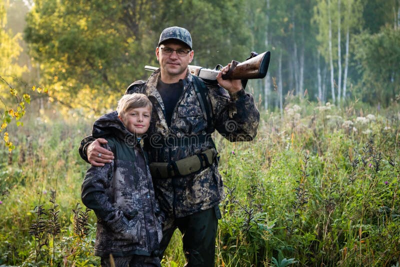 Father and son standing together outdoors with shotgun hunting gear.